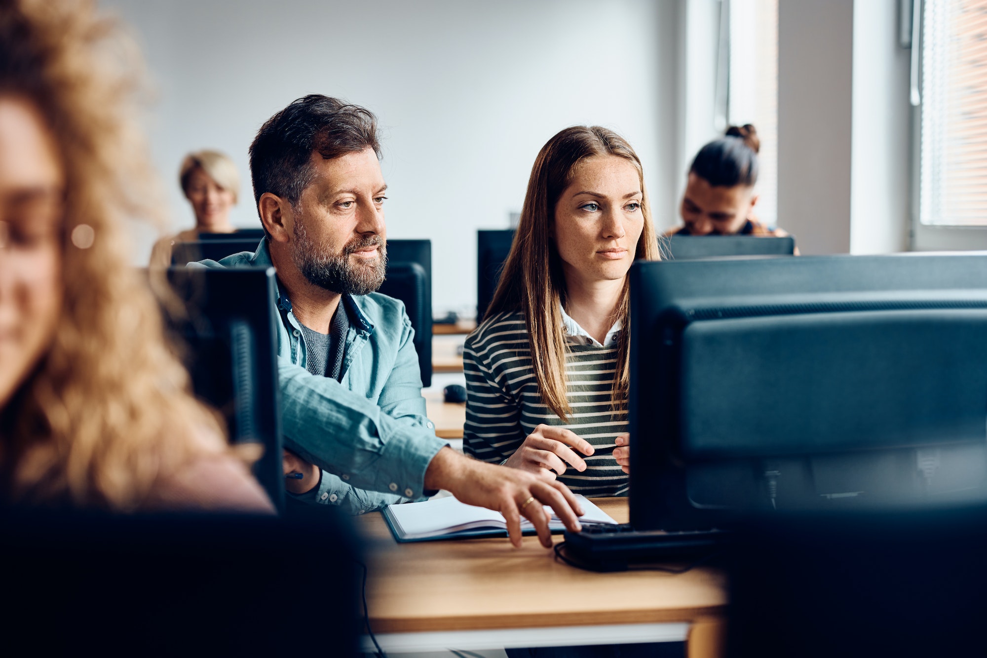 Adult students cooperating while e-learning on a computer in the classroom.