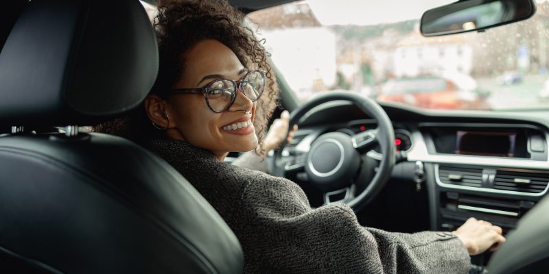 Woman driving car with one hand on steering wheel and another on gear lever and